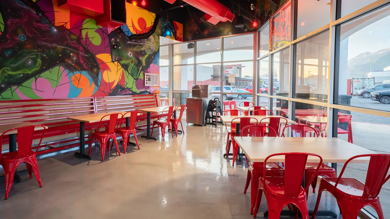 Spacious dining area with red chairs and tables at Dave’s Hot Chicken on E. University Pkwy in Orem, UT, showcasing colorful graffiti art.