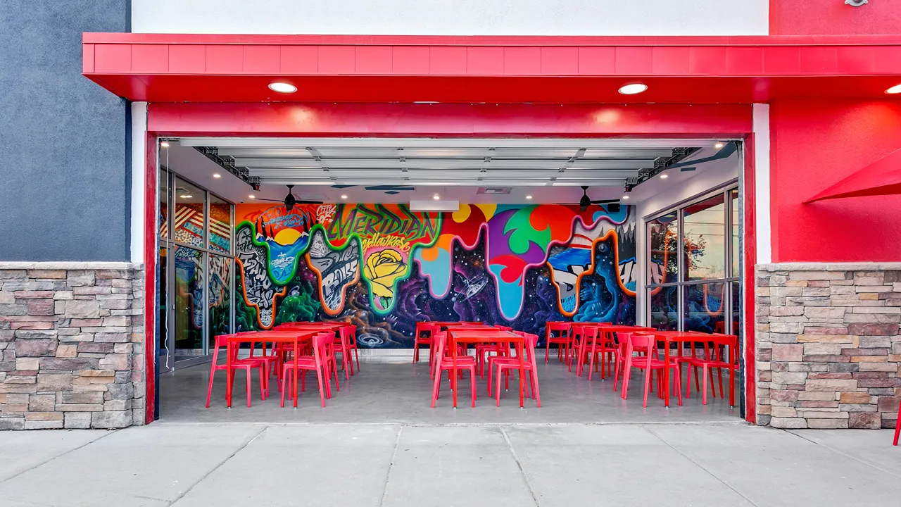 Spacious outdoor seating with red chairs and tables and a vibrant mural wall at Dave's Hot Chicken on Eagle Rd, Meridian, ID.