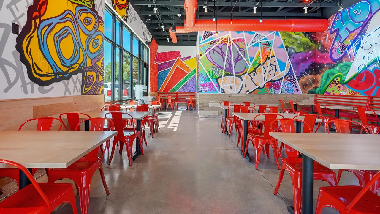 Bright interior dining area with colorful murals, red chairs, and large windows at Dave’s Hot Chicken in Salt Lake City, UT.