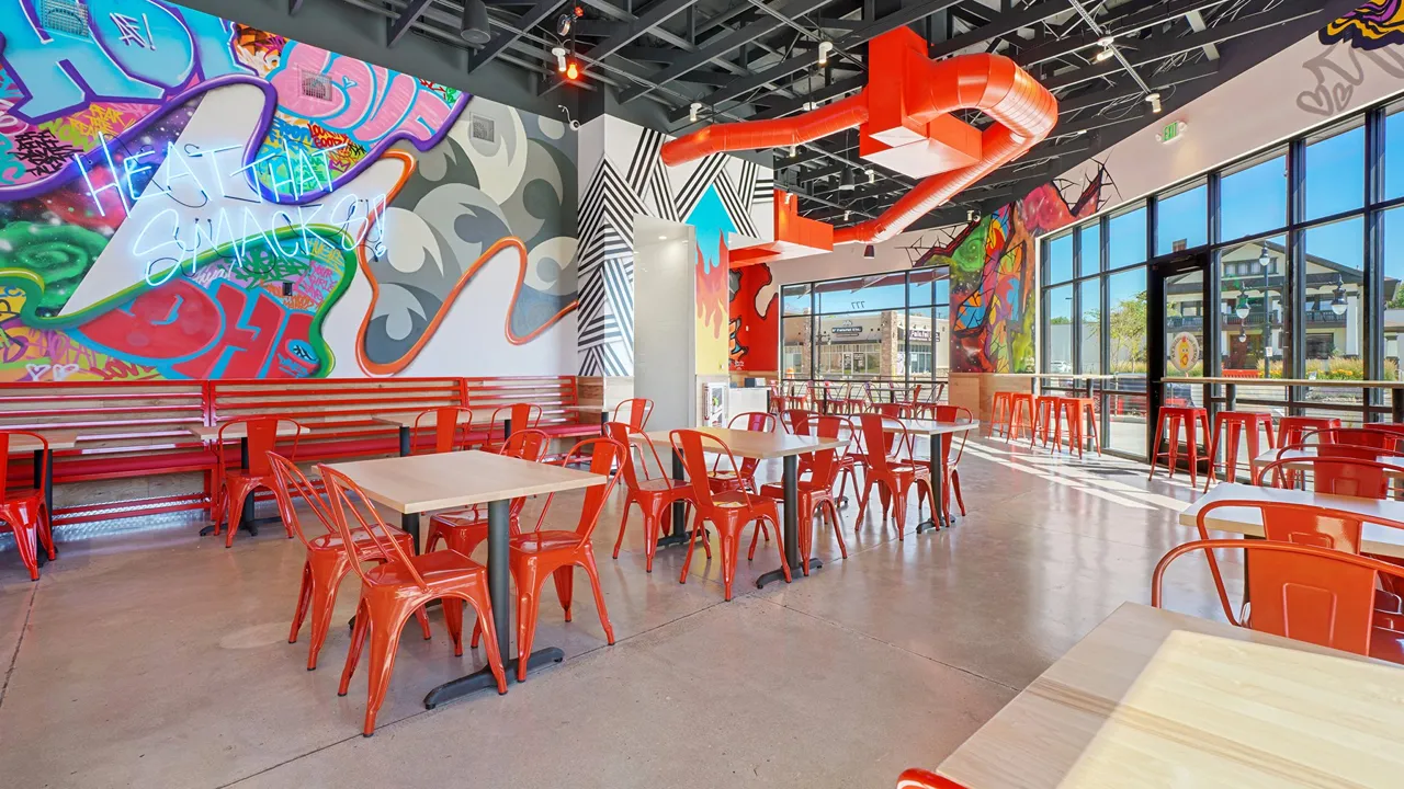 Interior seating with red chairs, wood tables, and artistic murals on the walls at Dave’s Hot Chicken in Salt Lake City, UT.