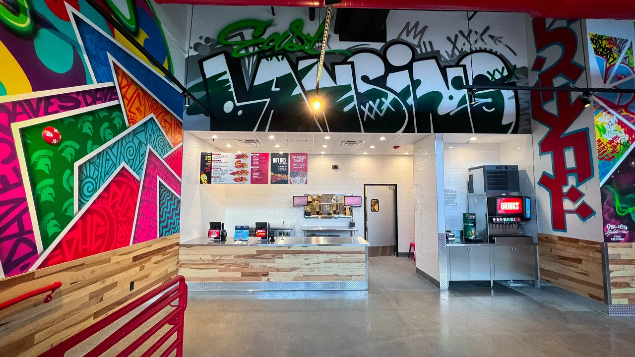 Wide shot of Dave's Hot Chicken interior, showing colorful graffiti-style murals, seating, and the order counter in East Lansing, MI.