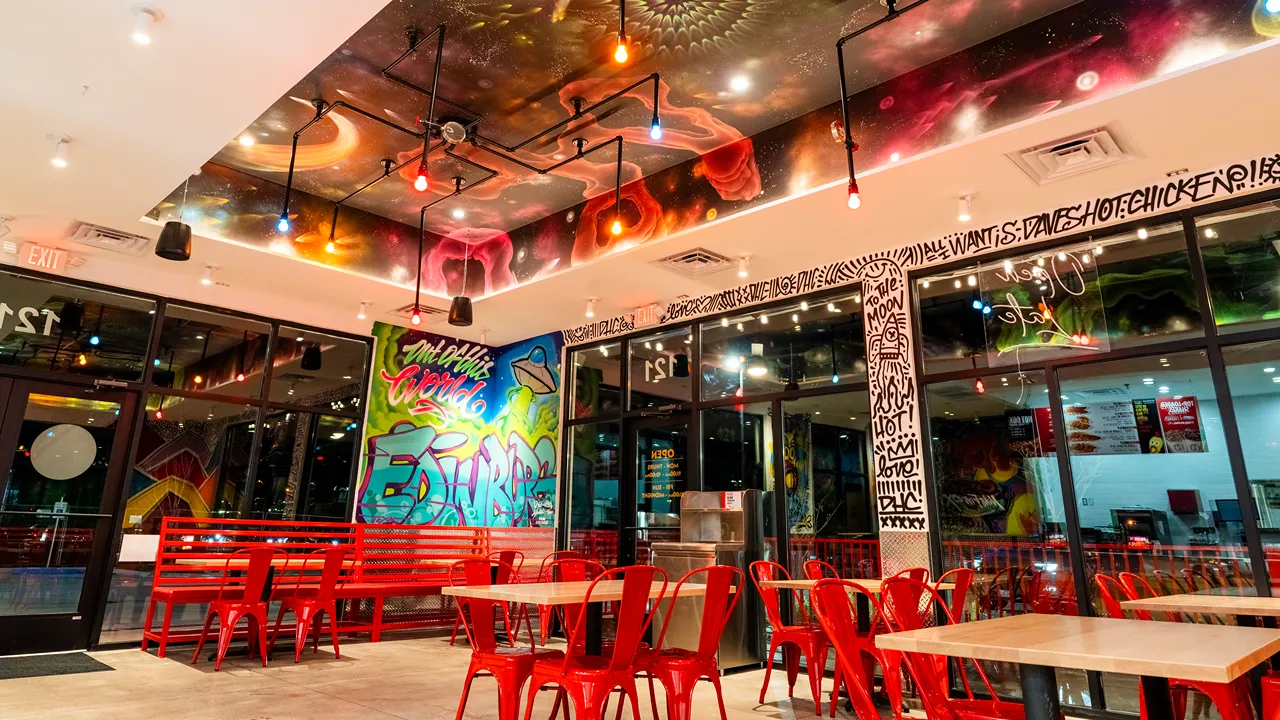 Red chairs, wooden tables with vibrant graffiti-style murals on the ceiling and walls inside Dave's Hot Chicken in Edinburg, TX.