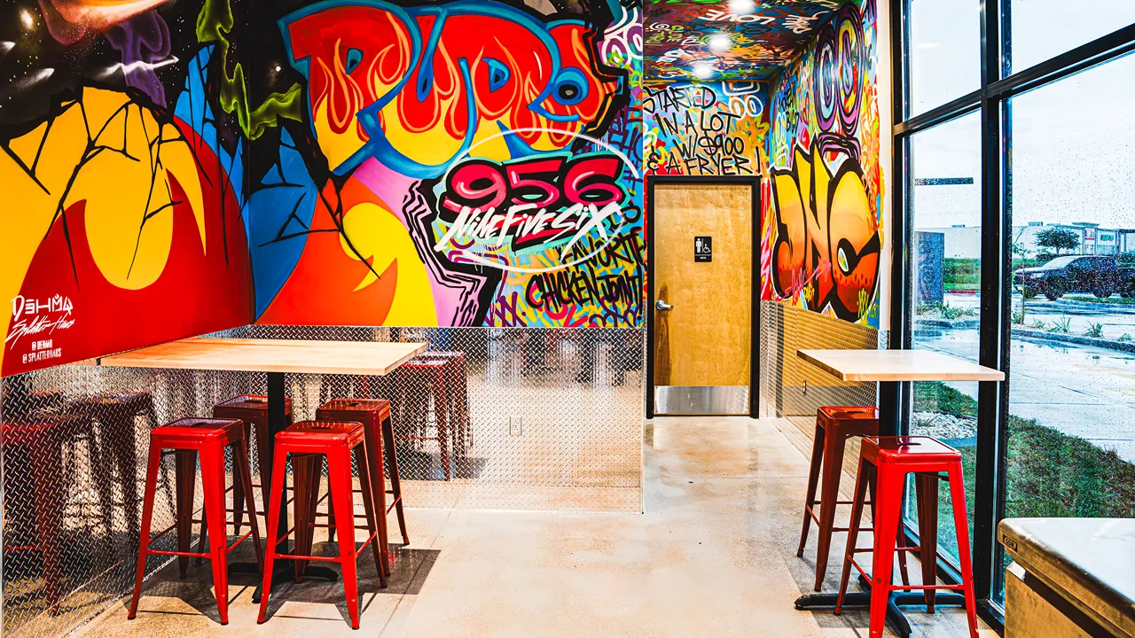 Vibrant seating area with high stools and graffiti murals, featuring bright colors, inside Dave's Hot Chicken in Edinburg, TX.