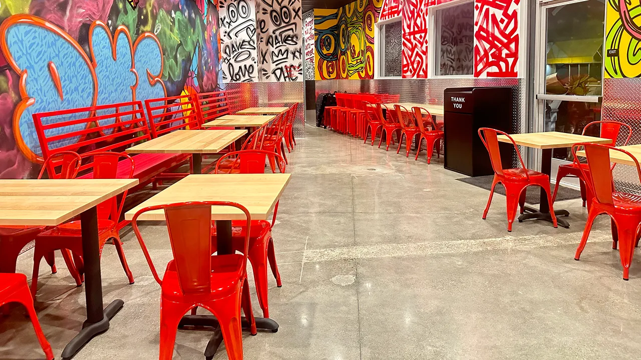 Interior seating area with wall art, red benches, and tables at Dave's Hot Chicken in El Cerrito Plaza, El Cerrito, CA.