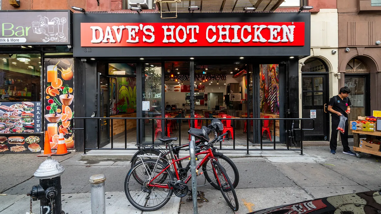 Exterior of Dave's Hot Chicken at 311 7th Ave, Brooklyn, NY with a bright red sign and bicycles parked outside.