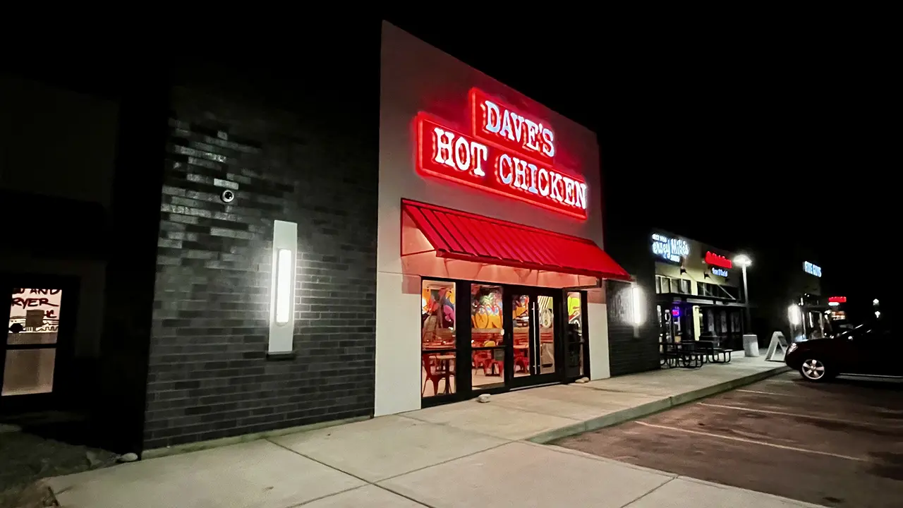 Exterior of Dave's Hot Chicken in Billings, MT, at night, with bright signage and a vibrant interior visible through the windows.