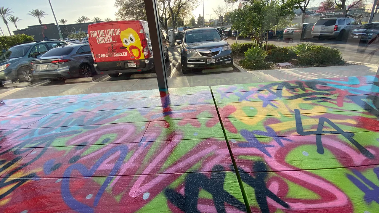 A colorful mural on the concrete floor outside the entrance of Dave’s Hot Chicken, N Victory Pl, Burbank, CA, with vibrant graffiti art.