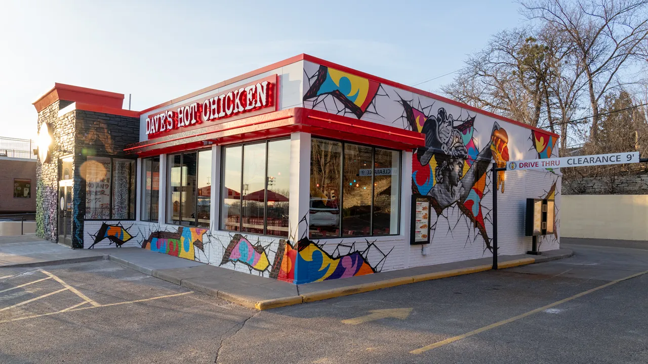 Daytime view of the Dave’s Hot Chicken on Ford Parkway, St. Paul, MN, showing the drive-thru area with bright exterior wall art.