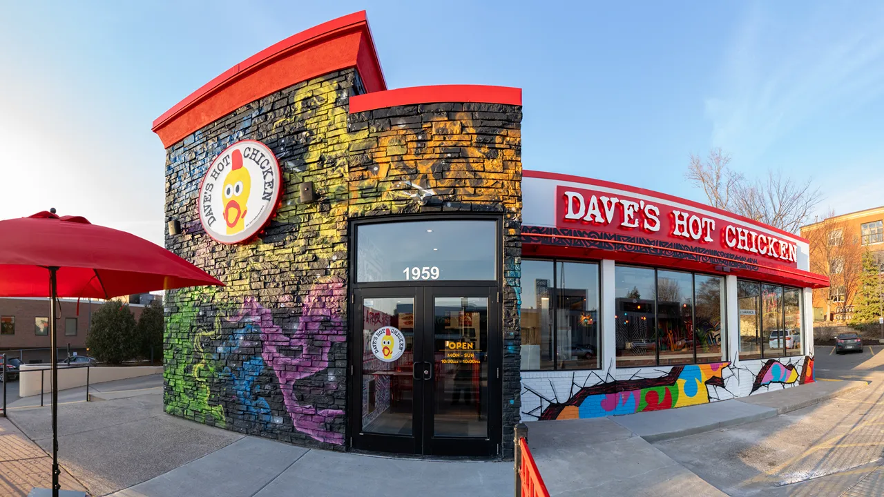 Front entrance of Dave’s Hot Chicken on Ford Parkway, St. Paul, MN, featuring colorful graffiti and bold signage.