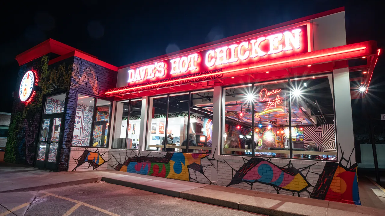 Nighttime exterior of Dave’s Hot Chicken on Ford Parkway, St. Paul, MN, with glowing neon signage and graffiti-style art on the building.