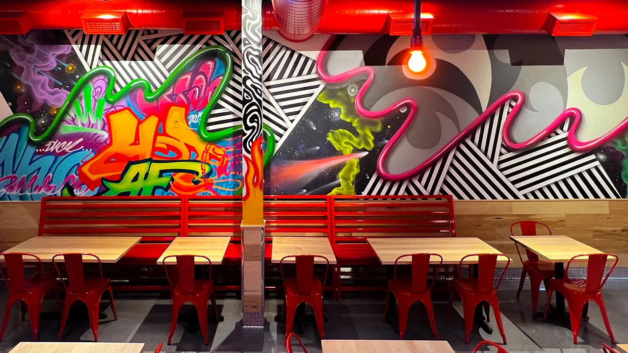 View of red bench seating and tables inside Dave's Hot Chicken on Fort Union Blvd, Midvale, UT, with striking wall graffiti.