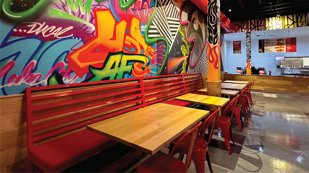 Red seating and wooden tables at Dave's Hot Chicken on Fort Union Blvd, Midvale, UT, with vibrant wall art in the background.