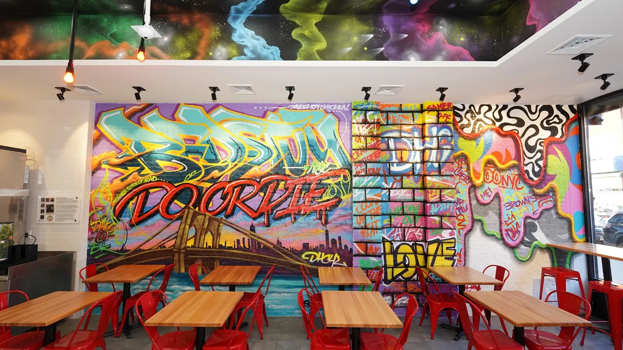 Graffiti mural inside Dave's Hot Chicken on Fulton St, Brooklyn, NY, featuring the Brooklyn Bridge and colorful seating.