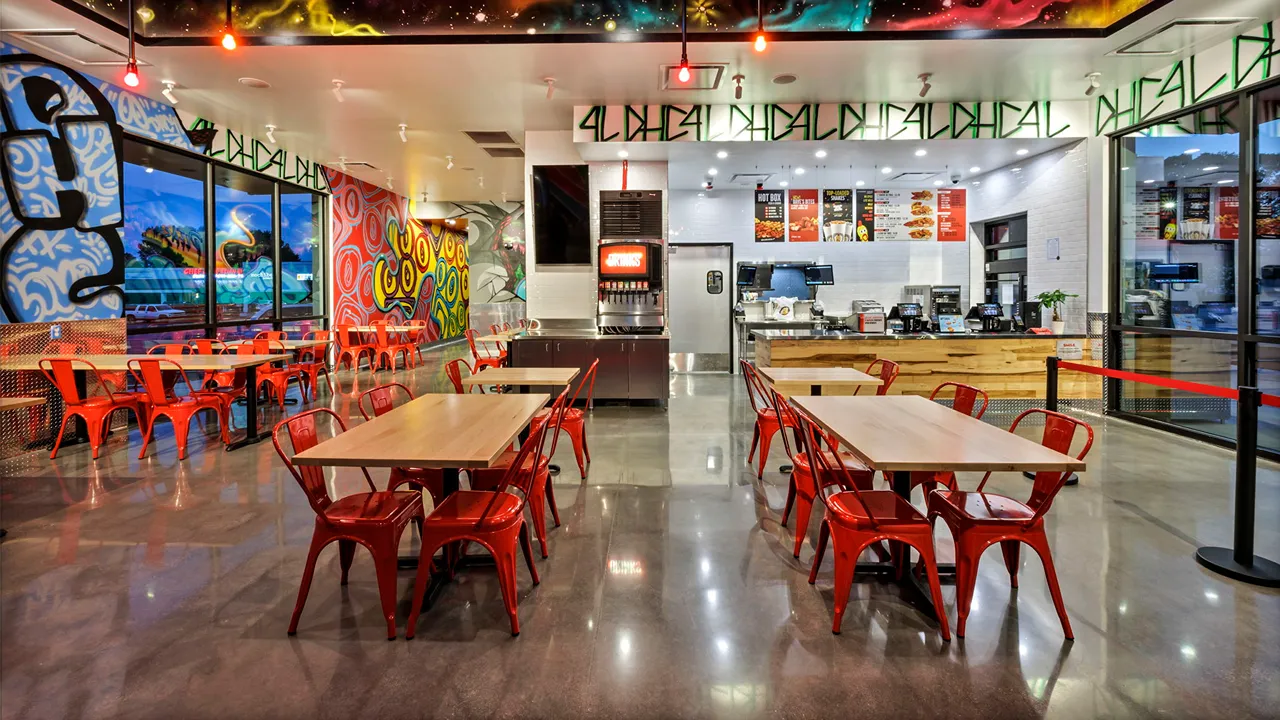 Bright, open seating area with red chairs and colorful murals inside Dave’s Hot Chicken restaurant in Greenville, SC.