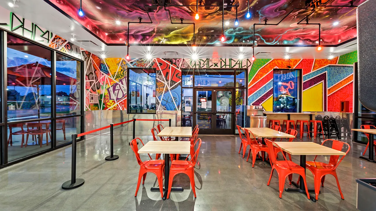 Vibrant dining area with modern seating, wall art, and large windows at Dave’s Hot Chicken in Greenville, SC.