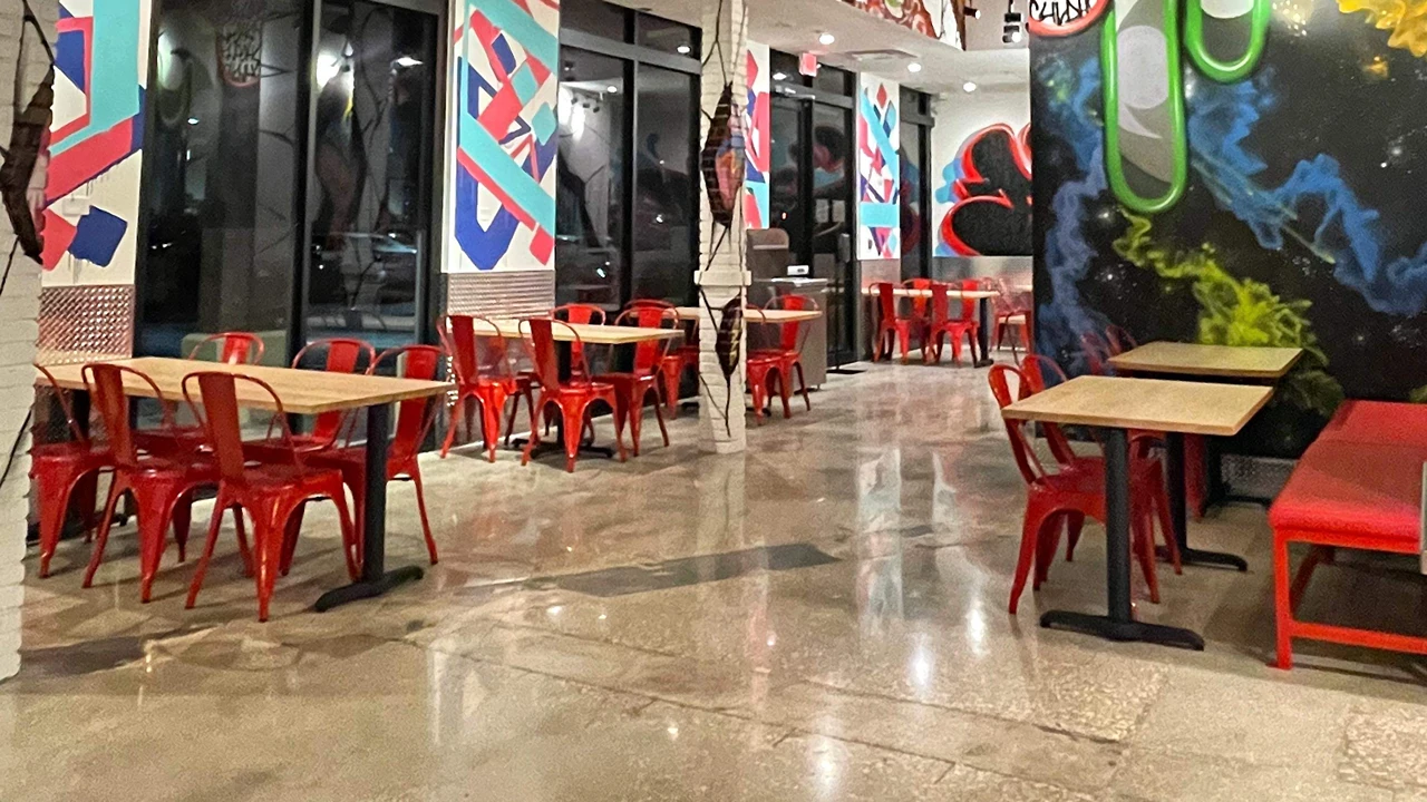 Red chairs and bench seating with wooden tables inside Dave's Hot Chicken in Altamonte Springs, FL, with colorful wall art.