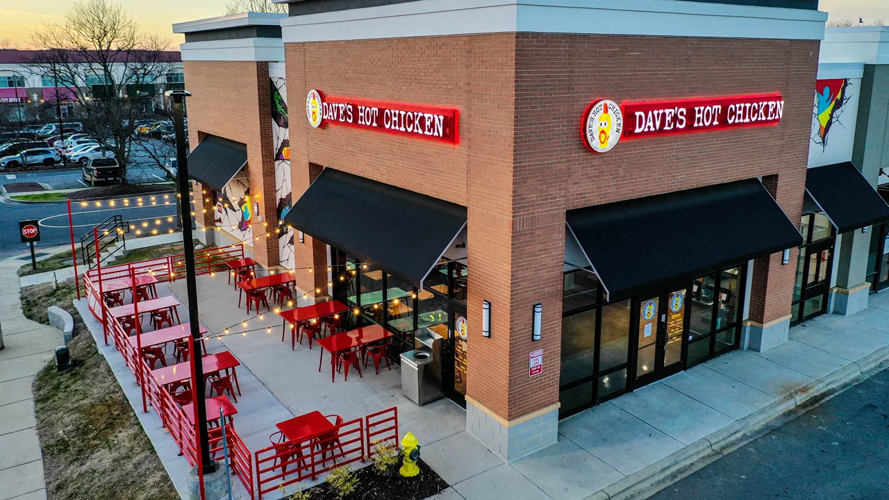 Side view of Dave’s Hot Chicken at J.M. Keynes Drive, University Place, Charlotte, NC, with string lights illuminating the outdoor seating area.