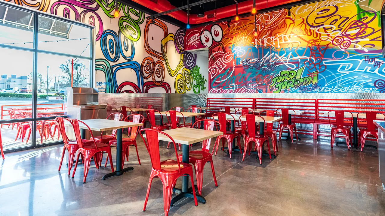 Interior of Dave’s Hot Chicken at J.M. Keynes Drive, University Place, Charlotte, NC, featuring colorful graffiti wall art and red seating.