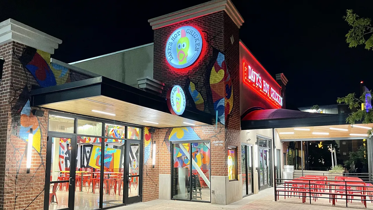 Nighttime view of Dave's Hot Chicken with bright red signage and outdoor seating on Johnny Bench Dr., Oklahoma City, OK.