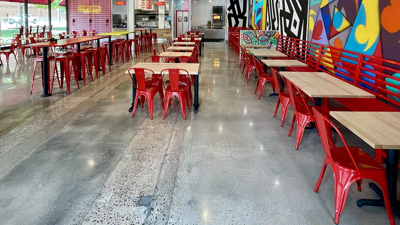 Long view of the dining area with red stools and tables, colorful wall murals at Dave's Hot Chicken on Johnny Bench Dr., Oklahoma City, OK.