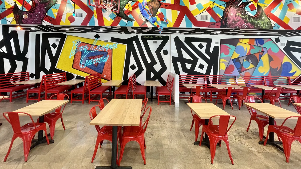 Bright seating area with red chairs and booths, featuring wall art at Dave's Hot Chicken on Johnny Bench Dr., Oklahoma City, OK.