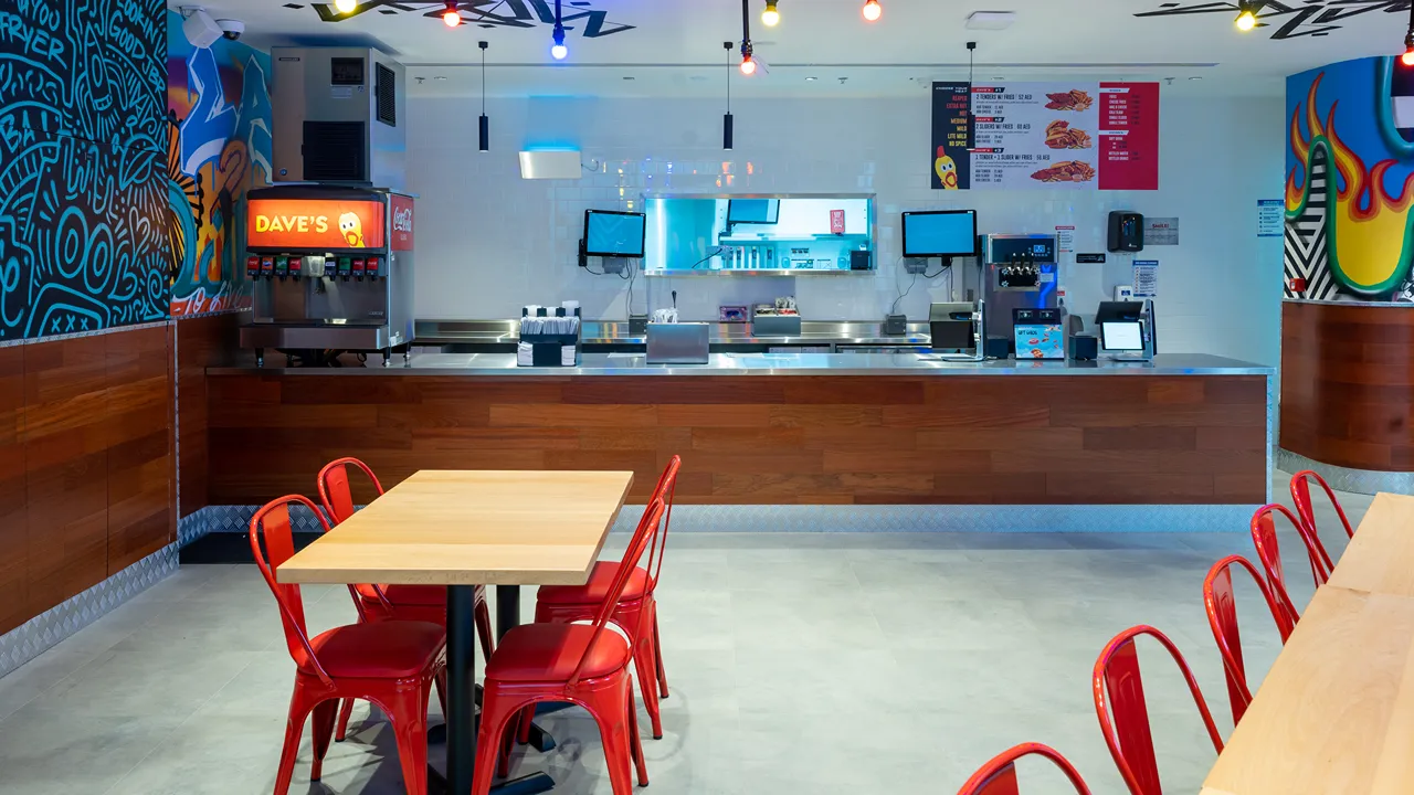 Clean and modern counter area with vibrant wall murals and red seating inside Dave's Hot Chicken, Dubai, UAE.