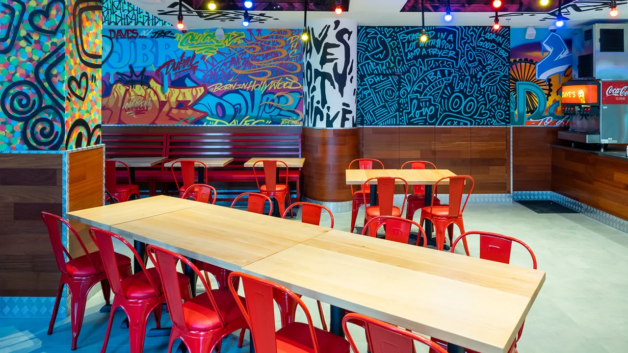 Seating area with red chairs, long wooden tables, and graffiti-style murals inside Dave's Hot Chicken, Dubai, UAE.