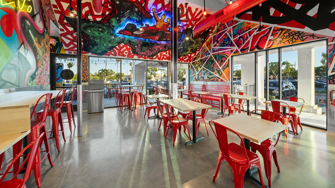 Bright and open interior seating area with red chairs and large murals at Dave's Hot Chicken on E Los Coyotes Diagonal, Long Beach, CA.