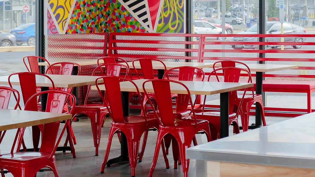 Red chairs and tables at Dave's Hot Chicken, Loucks Rd., York, PA, with colorful wall art visible in the background.