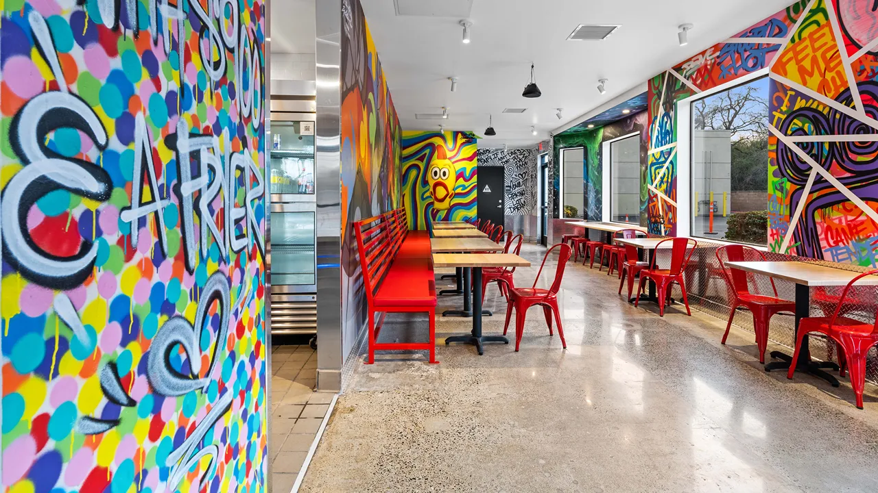 Bright interior with red stools and tables, surrounded by vibrant graffiti murals at Dave's Hot Chicken in Fair Oaks, CA.