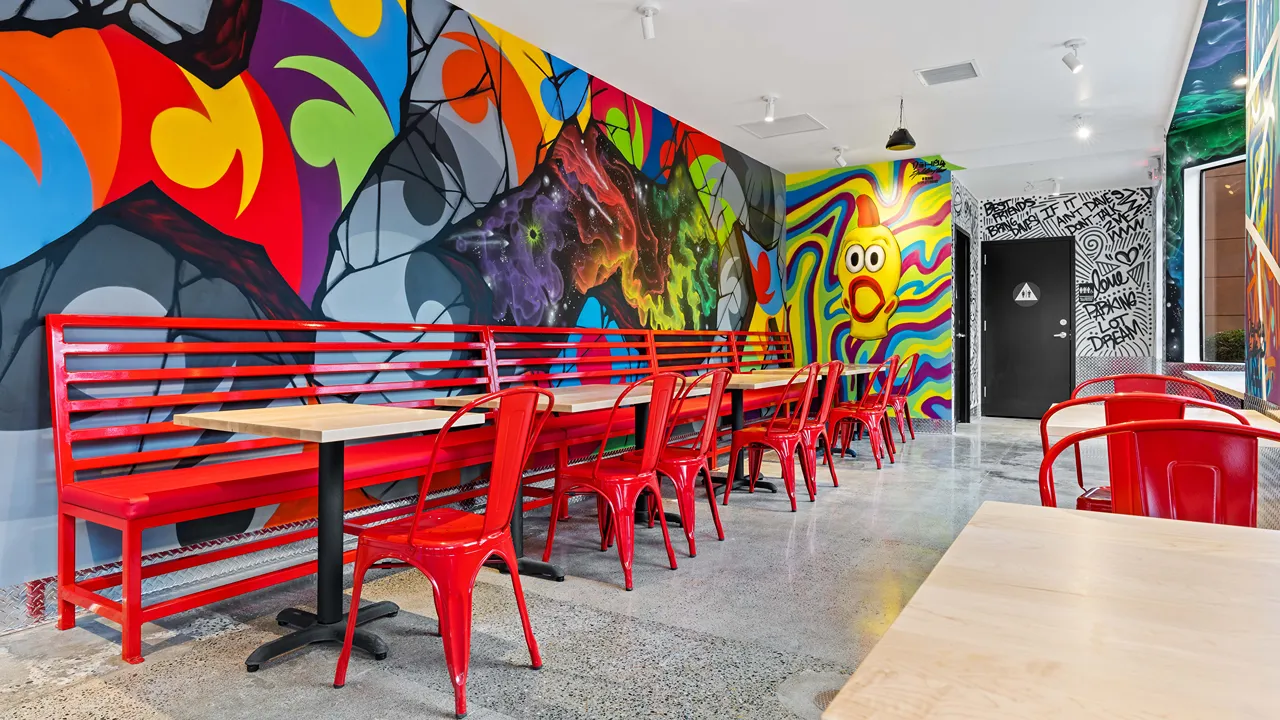 Interior view with red chairs and tables, featuring a colorful mural at Dave's Hot Chicken in Fair Oaks, CA.