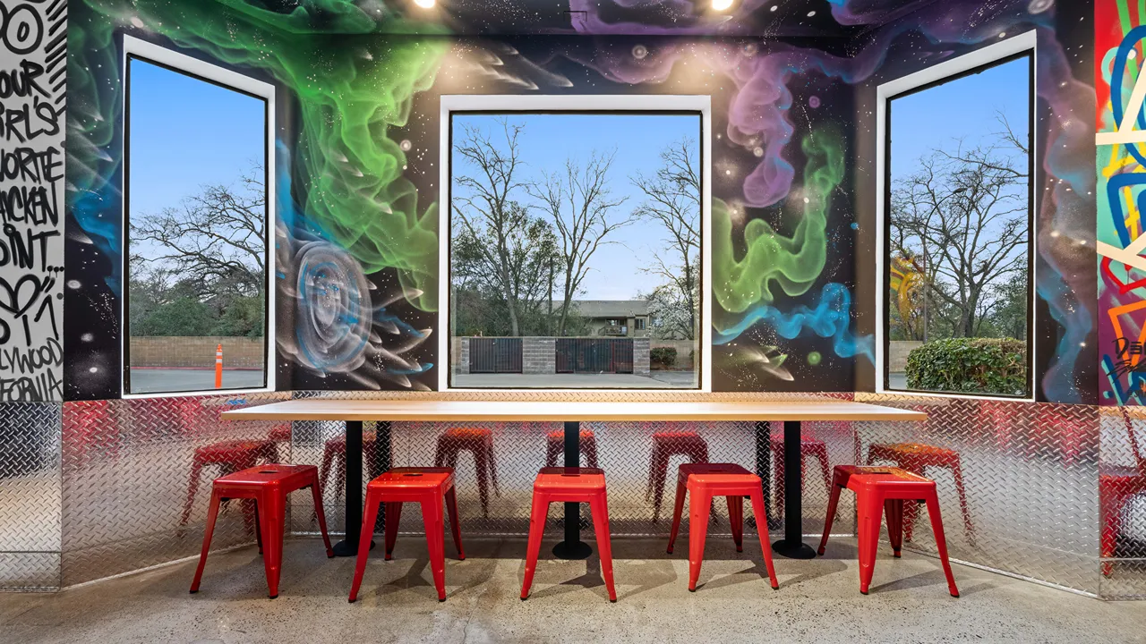 Interior wall art with graffiti and abstract murals, accompanied by seating at Dave's Hot Chicken in Fair Oaks, CA.