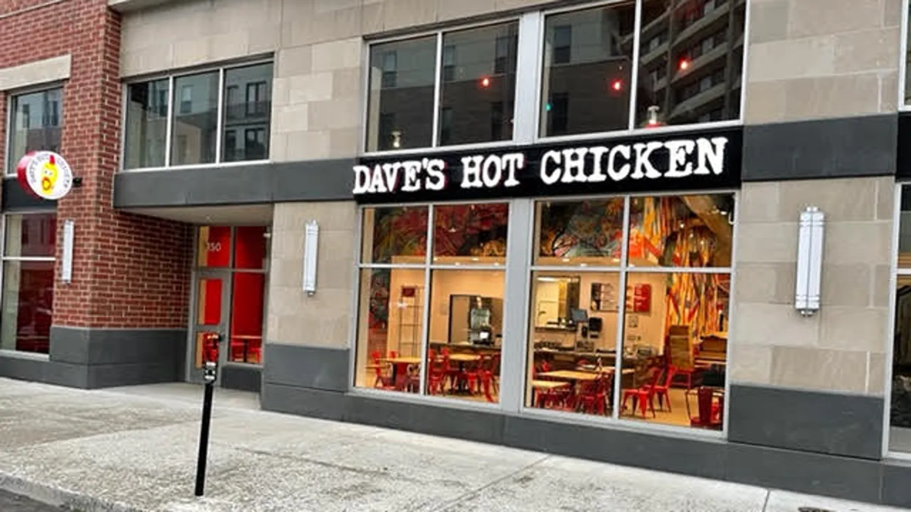 Exterior view of Dave’s Hot Chicken on Massachusetts Ave, Indianapolis, in the Penrose district with illuminated signage and large windows.