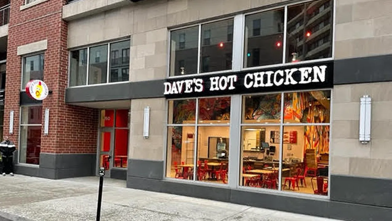 Exterior view of Dave’s Hot Chicken on Massachusetts Ave, Indianapolis, in the Penrose district with large windows and red seating inside.