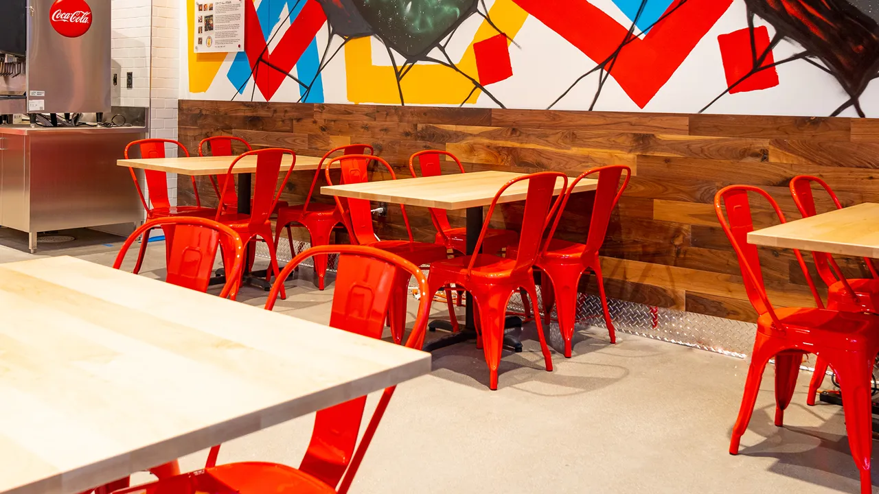 Interior seating area with red chairs, light wooden tables and a colourful wall at Dave’s Hot Chicken on Massachusetts Ave, Indianapolis, in the Penrose district.