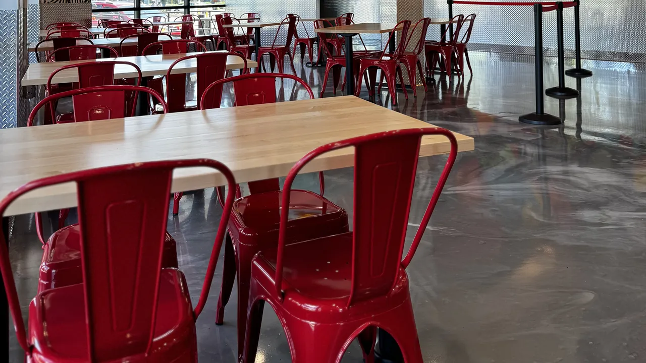 Seating area with red chairs and wooden tables on a polished marbelled style floor inside Dave's Hot Chicken on Mystic Valley Pkwy, Medford, MA.