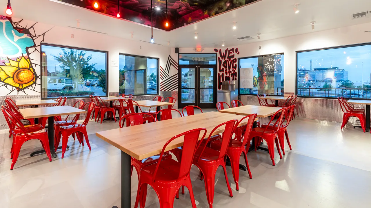 Colorful wall art inside Dave's Hot Chicken on Metcalf Avenue, Overland Park, KS, with tables and chairs in the seating area.