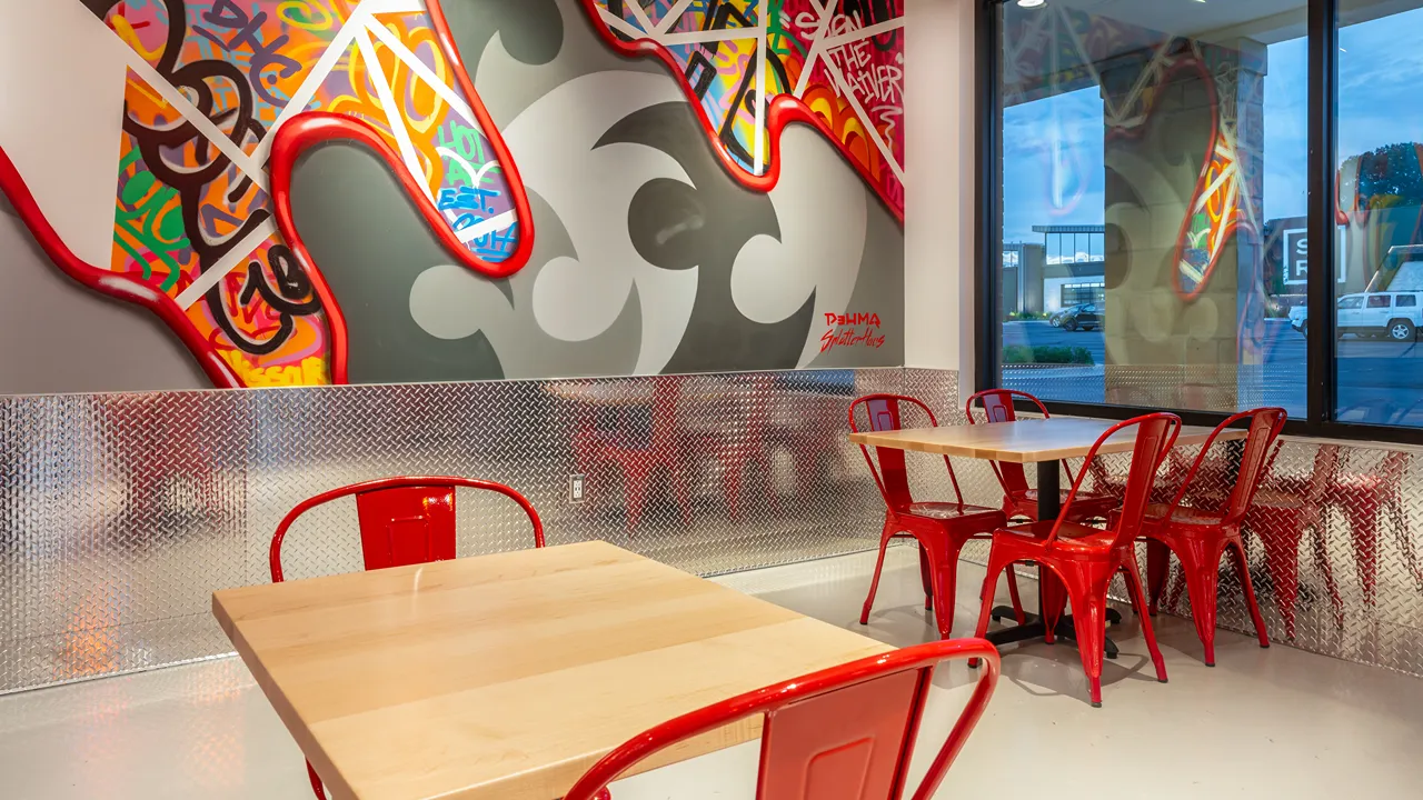 Seating area with wall art and red chairs inside Dave's Hot Chicken on Metcalf Avenue, Overland Park, Kansas.