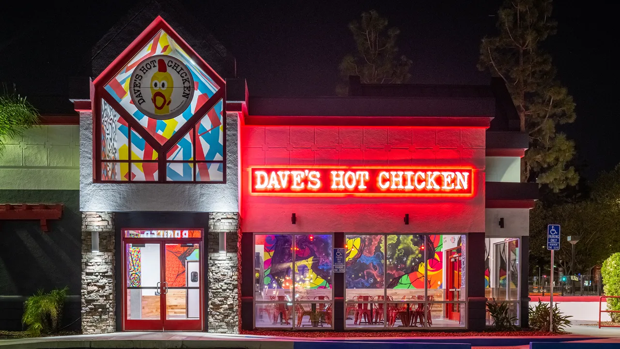 Nighttime exterior view of Dave's Hot Chicken with bright red signage and colorful windows on Milliken Ave, Ontario, CA.