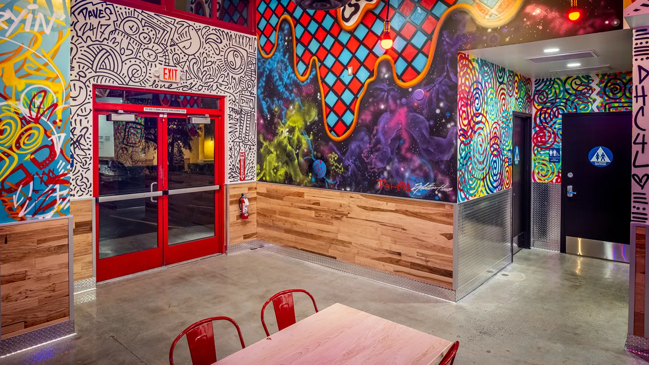 Indoor dining area with graffiti-style art and red seating near the windows at Dave's Hot Chicken, Milliken Ave, Ontario, CA.