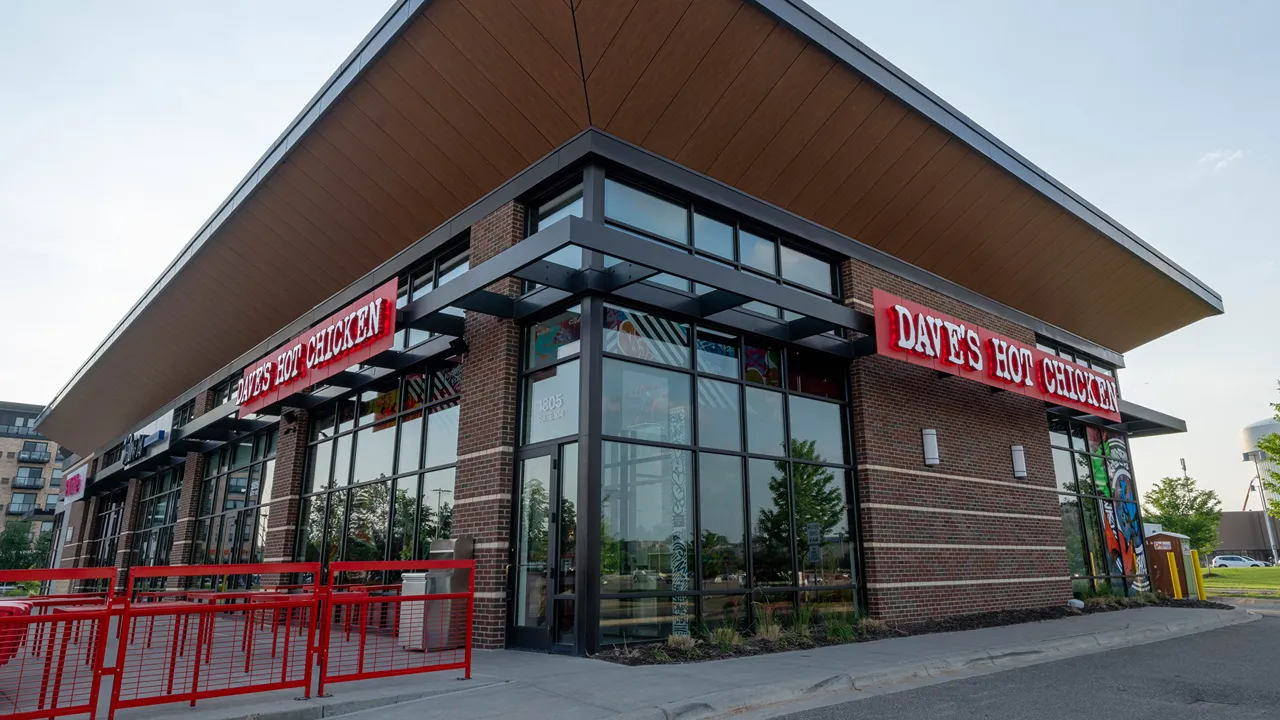 Angled view of Dave's Hot Chicken restaurant on Plymouth Rd, Minnetonka, MN, showing glass windows and the modern brick design.