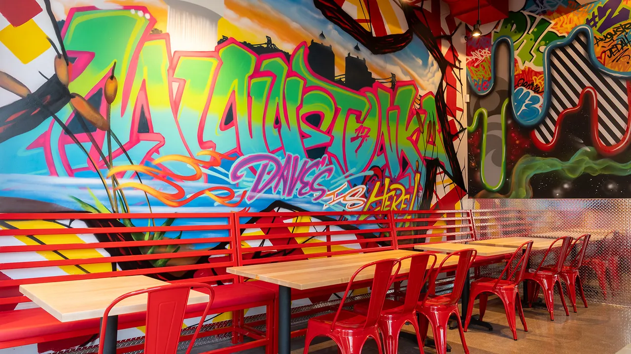 Colorful 'Minnetonka' mural with Dave's Hot Chicken branding inside the Plymouth Rd, Minnetonka, MN location, featuring red seating.