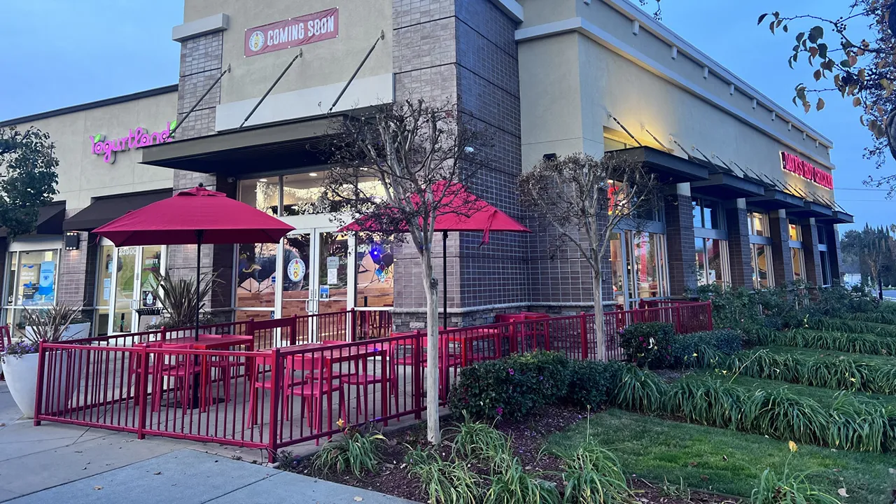 Exterior view of Dave's Hot Chicken on Monument Blvd, Pleasant Hill, CA, featuring red patio seating and nearby shops.