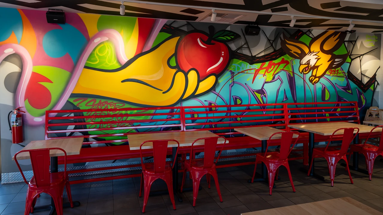 Vibrant mural inside Dave's Hot Chicken in Apple Valley, MN, with red seating and colorful artwork featuring an apple and a hawk.