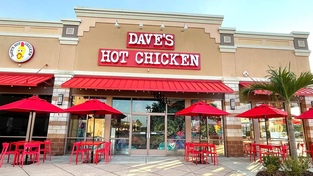 Exterior facade and outdoor seating area at Dave's Hot Chicken on N. Alafaya Trail, Waterford Lakes, Orlando, FL, with red tables and chairs.