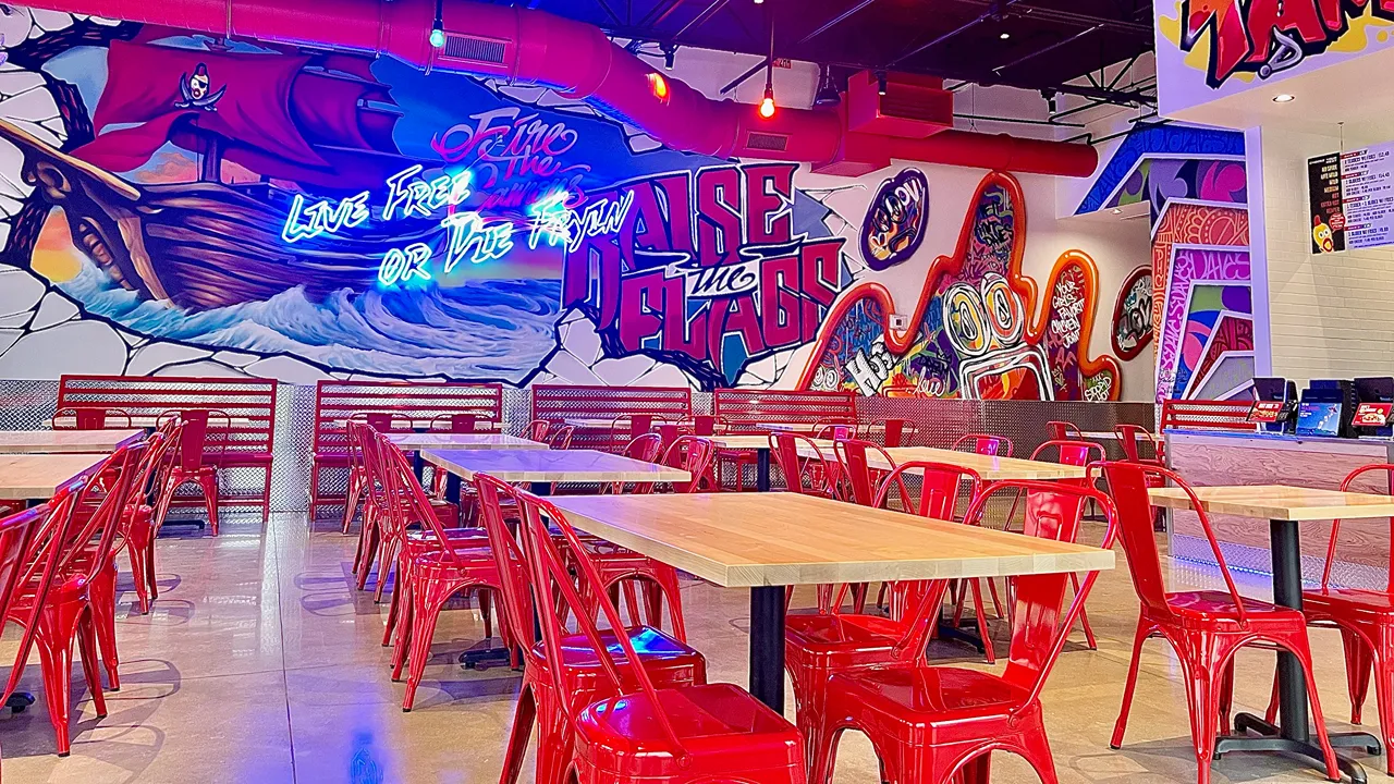 Vibrant wall art and seating area inside Dave's Hot Chicken on N Dale Mabry Hwy in Tampa, FL, showcasing red chairs and tables