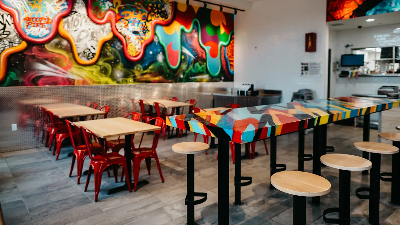 Seating area inside Dave's Hot Chicken on N. Eddy St., South Bend, IN, with red chairs and tables beneath a colorful mural.