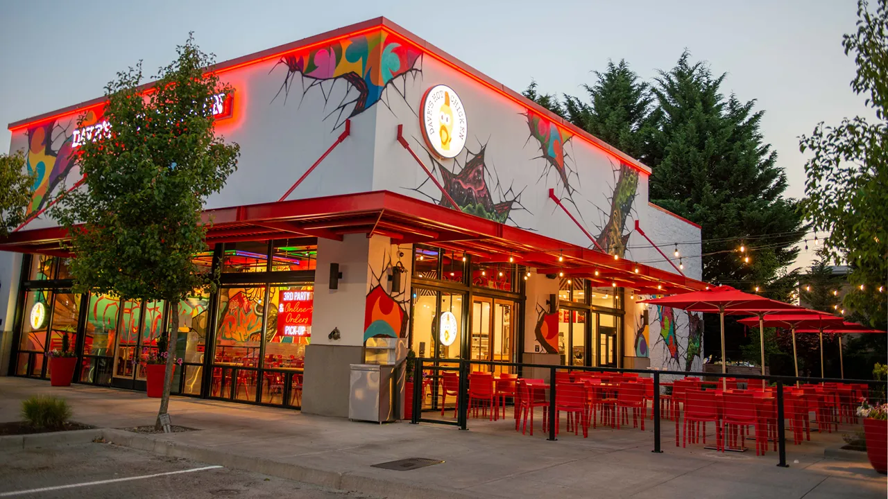 Exterior view of Dave's Hot Chicken in Hazel Dell at night with red accents and outdoor seating, located on NE 6th Ave, Vancouver, WA.