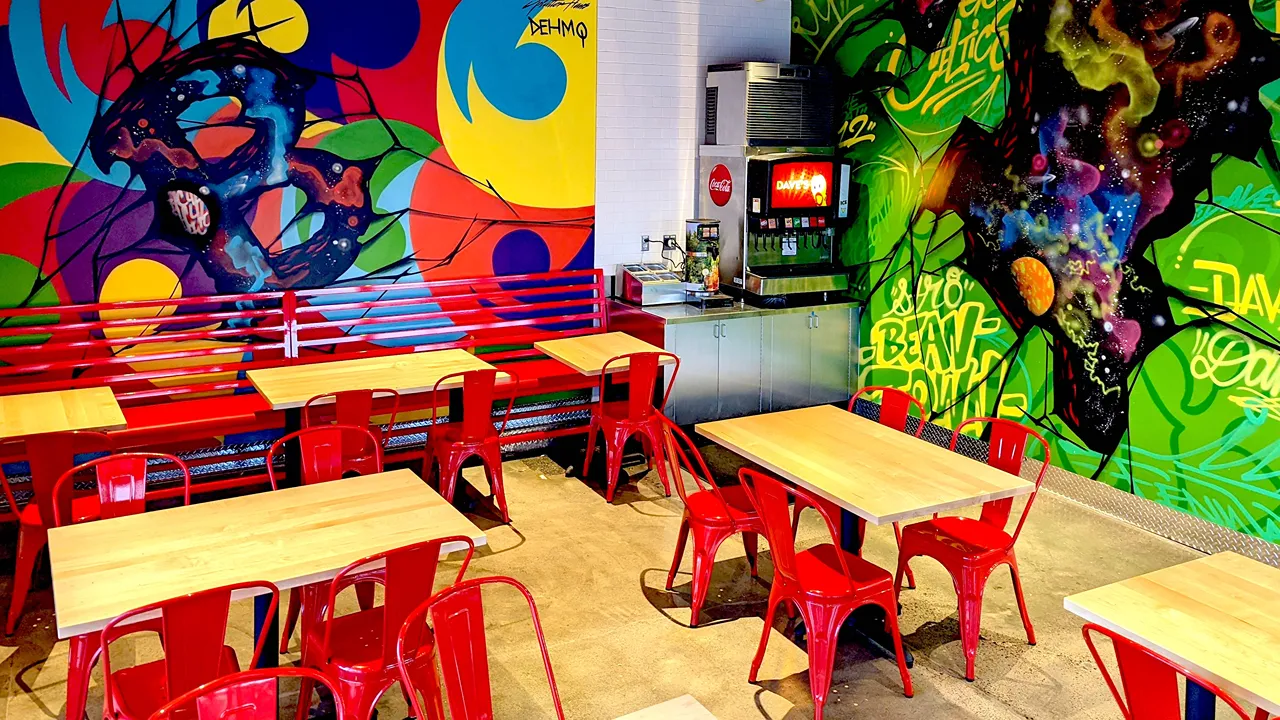 Bright dining area with red chairs and colorful murals with a drink fountain at Dave's Hot Chicken on Needham St., Newton, MA.