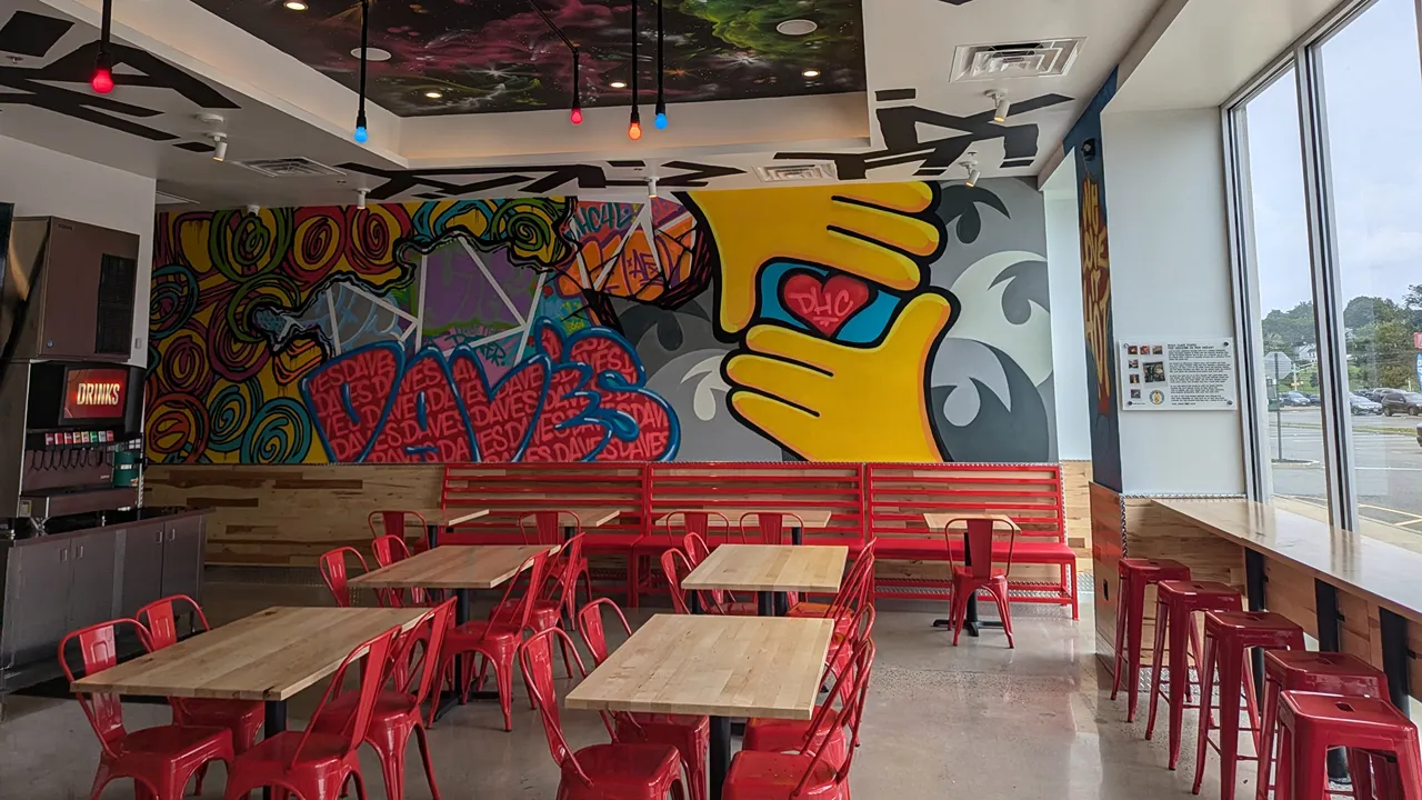 Inside Dave's Hot Chicken on Passaic Ave, Kearny, NJ, showcasing colorful wall art and red seating.